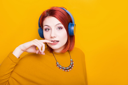 Sexy redhead woman wearing blue headphones on yellow backgroundの写真素材