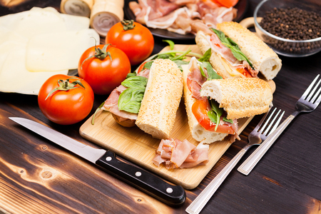 Four sandwiches on wooden board next to ingredients that it was made ofの写真素材