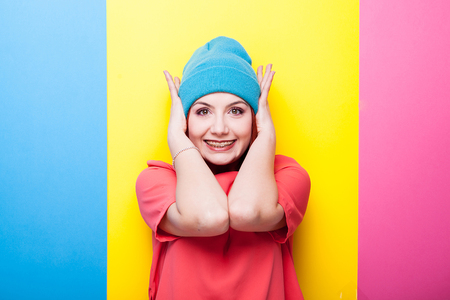 Hipster teenager in blue hat smiling at camera on three colored background, yellow, blue and pinkの写真素材