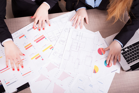 Two women with a lot of charts on the table looking at themの写真素材