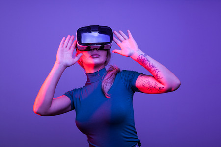 Tattoed sexy woman wearing a virtual reality VR head set on blue background