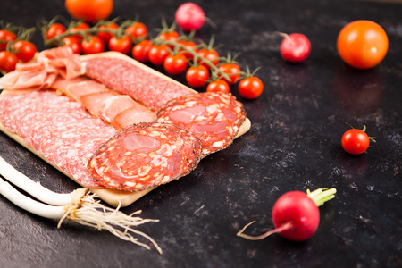 Meat appetizers on wooden board next to cherryes and tomatoes on dark wooden backgroundの写真素材