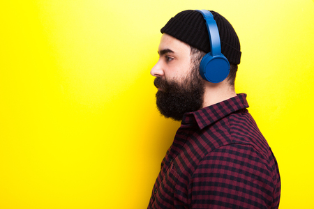 Bearded hipster man wearing a black hat and listening to music through wireless headphonesの写真素材