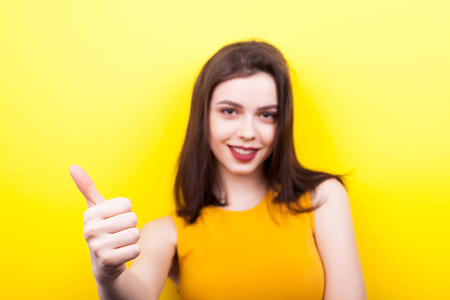 Beautiful woman showing thumbs up on yellow backgroundの写真素材