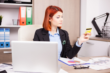Businesswoman in her office looking at a credit card for online shoppingの写真素材