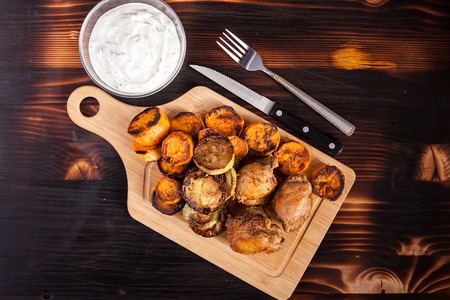 Top view of fried chicken next to grilled sweet potatoes, quash and sour cream souce on wooden backgroundの写真素材