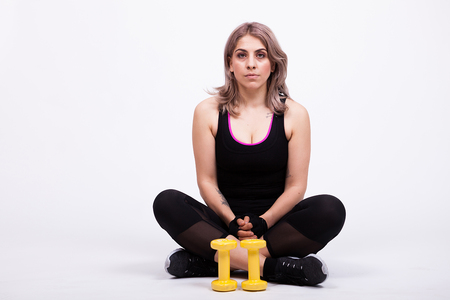 Woman in sport clothes lying down with two small dumbbells beside her. Studio photo. Gray backgroundの写真素材