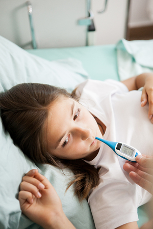 Doctor taking body temperature of her patient in hospital roomの写真素材