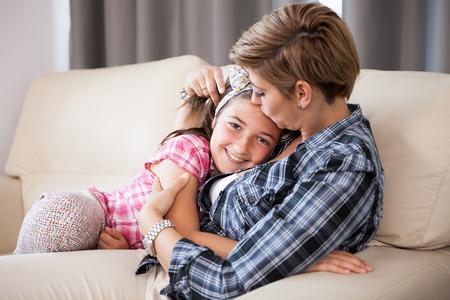 Happy mother and child daughter holding each other in arms on the couchの写真素材