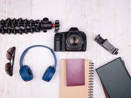 Flat lay top view of traveler accessories on white wooden background. DSLR and action camera, blue...