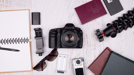 Flat lay top view of traveler accessories on white wooden background. DSLR and action camera, paper...