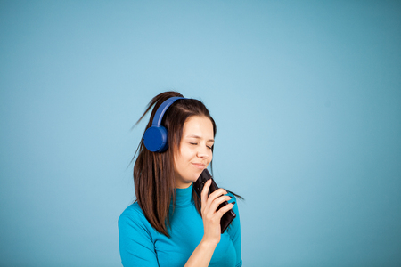 Cute young woman singing on her phone in studio on blue backgroundの写真素材