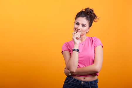 Portrait of reflective beautiful woman wondering over yellow background in studioの写真素材