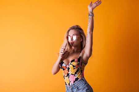 Cute young woman singing on her phone in studio over yellow background with sunglassesの写真素材