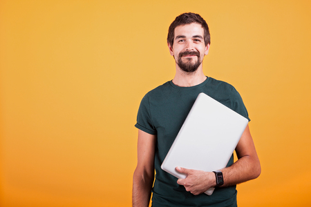 Happy smiling attractive man with a laptop in his hands isolated on orange background. Wireless technology for communicationの写真素材