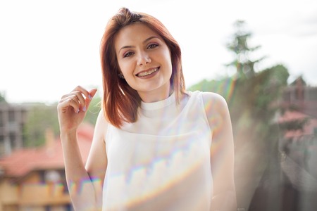 Portrait of gorgeous redhaired woman in summer rays at a balcony