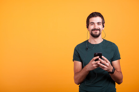 Happy smiling man with headphones on listening music on his smartphone isolated on yellow...