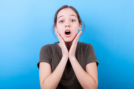 Surprised teenager girl on blue background in studio photoの写真素材