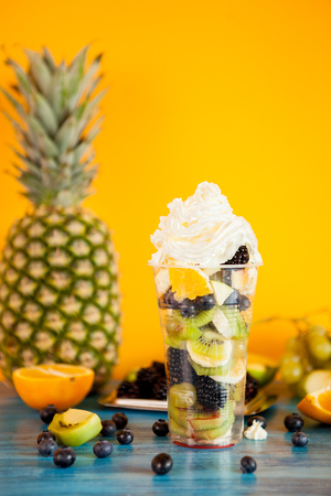 Cup full of tasty fruits topped with whipped cream over a wooden table. Summer delicious desertの写真素材