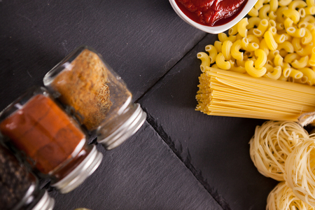Italian uncooked pasta next to bottle with spices and bowl with tomato souce. Top view with selective focusの写真素材