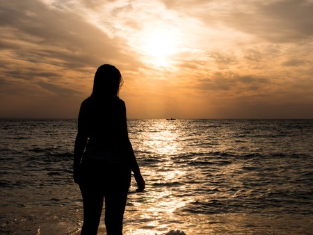 Woman silhouette watching sun on the beach at sunset.. Tourist girl on beach holidayの写真素材