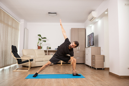 Attractive man trying extended side Yoga poses on his house floor. Athletic training.の写真素材