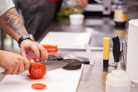 Chef slicing tomatoes for burger in kitchen restaurantの写真素材