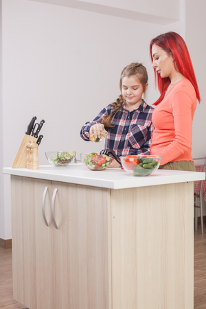 Mother telling her daughter how much oil the salad should have. Oil bottle.の写真素材