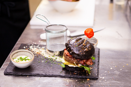 Black burger with french fries on stone cutting board.In kitchen restaurantの写真素材