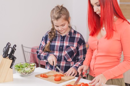Beautiful mother slicing tomatoes for salad. Smiling at her daughter.の写真素材