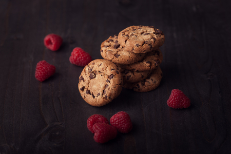 Chocolate chip cookies on dark old wooden table with red raspberry. Tasty snack.の写真素材