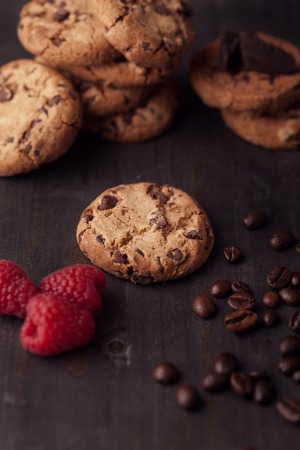 Chocolate chips cookies with red raspberries and coffee beans on dark old wooden table. Fresh out of the oven.の写真素材
