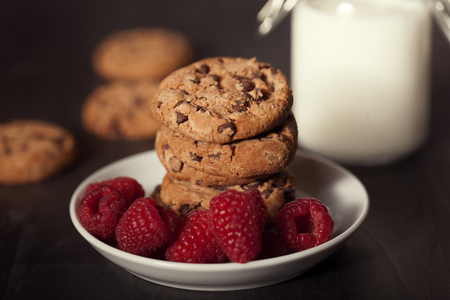 Chocolate chip cookies on white plate dark old wooden table with red raspberry and milk. Delicious breakfast.の写真素材