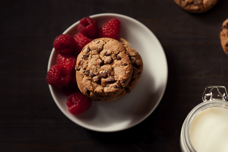 Top view of Chocolate chip cookies on white plate dark old wooden table with red raspberry. Healthy eating.の写真素材