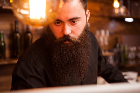 Handsome bartender checking the orders on his laptop. Hipster pub.の写真素材
