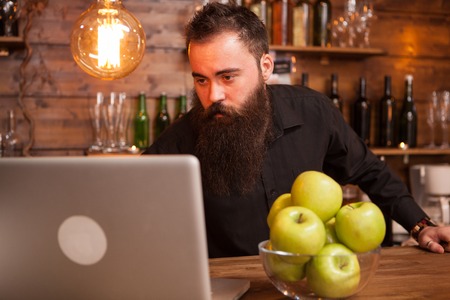 Handsome bartender checking the orders on his laptop. Hipster pub.の写真素材