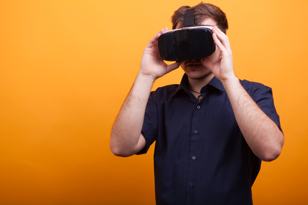 Funny good looking young man in blue shirt and his VR headset over yellow background. New gadgetの写真素材