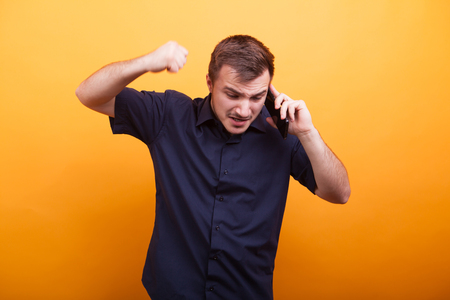 Young man in rage talking on mobile phone over yellow backgroundの写真素材