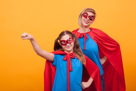 Little girl dressed like superheros holding her fist up in the air with her mother over eyellow...
