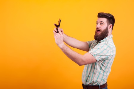 Hipster bearded man making a selfie over yellow background. Stylish beard. Cheerful young man.