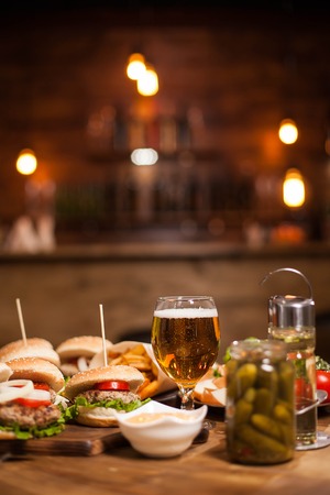 Mini burgers with a big glass of golden beer next to a jar of pickles. Vintage restaurant.の写真素材