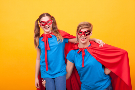 Superhero mother holding her little girl on her arm over yellow backgroundの写真素材