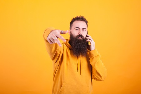 Cool bearded man looking at the camera and talking on the phone over yellow background. Handsome man. Confident man.の写真素材