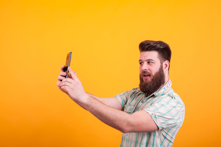 Hipster bearded man having a video call on his phone over yellow background. Expressive man.の写真素材