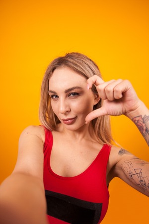 Gorgeous caucasian in red swimming suit holding camera and making a selfie over yellow backgroundの写真素材