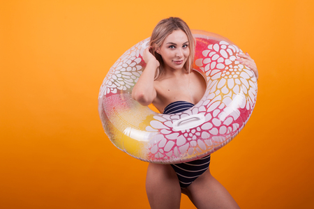 Thrilled beautiful woman with blue swimming suit playing with her hair and looking at the camera over yellowの写真素材