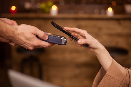 Cropped image of woman paying with mobile phone technology in a coffee shop. Woman using mobile...