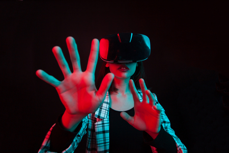 Pretty young girl wearing a virtual reality headset and touching something in studio over black background. Modern lifestyle of reality.の写真素材