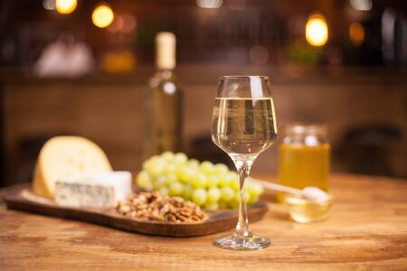 Photo of a sparkling white wine on a rustic wooden table in a vintage pub. Tasty cheese. Delicious grapes. Walnuts.の写真素材