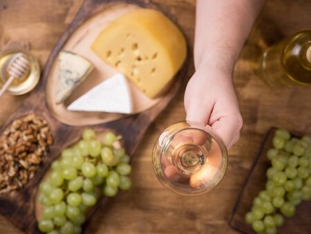 Top view of mens hand holding a glass of wine next to various cheeses.の写真素材